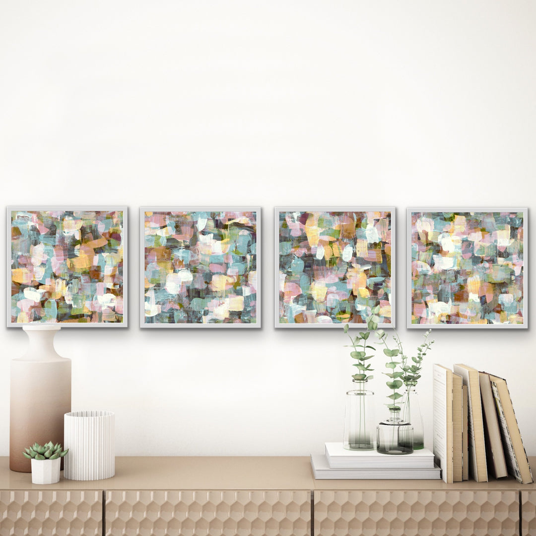 Four hand-painted abstract white  framed art prints displayed in a row above a table.  The four paintings have coordinating colors and style with slightly different designs.