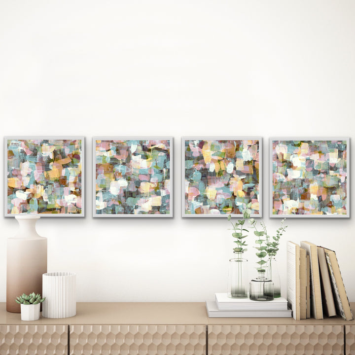 Four hand-painted abstract white  framed art prints displayed in a row above a table.  The four paintings have coordinating colors and style with slightly different designs.